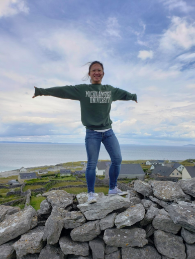 A woman stands on a stack of rocks, with her arms out.