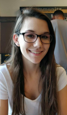 A woman in a white shirt with glasses is smiling at a camera.