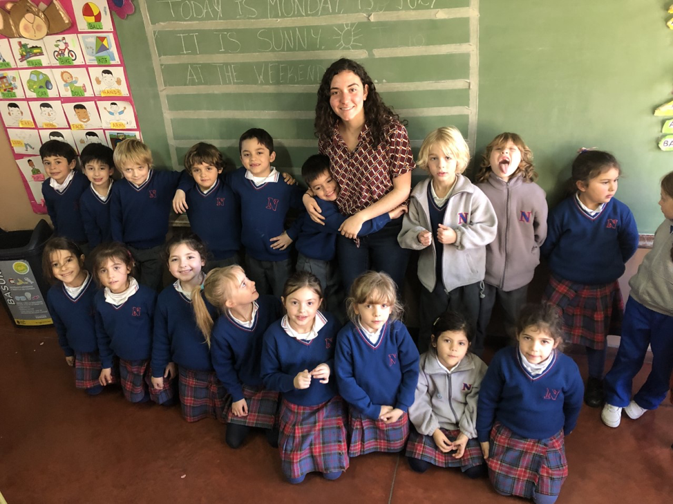 woman with shoulder-length dark hair posing with 18 children in matching outfits 