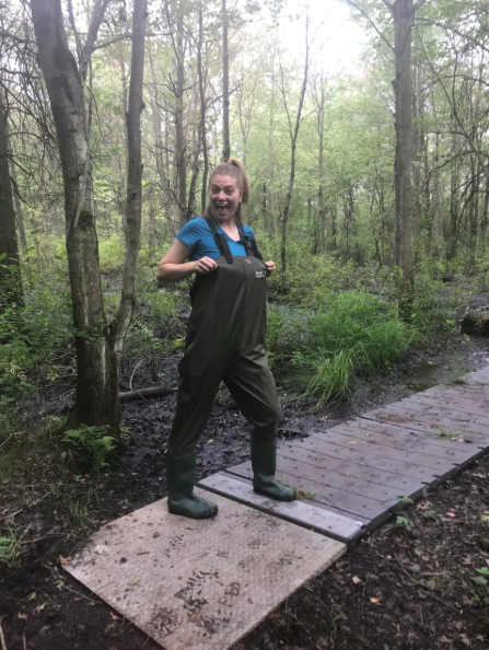 A woman is in waders on a wooden trail in the woods. 