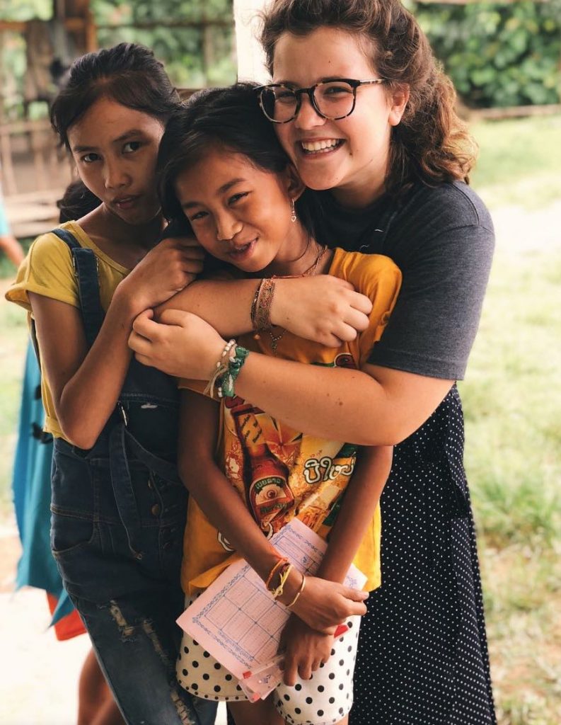 Photo of three girls hugging each other with two wearing yellow short sleeve shirts and the other wearing a grey one