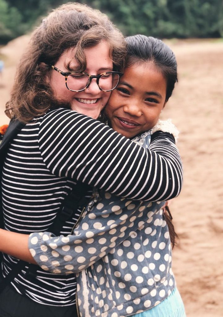 Photo of two girls hugging each other with left girl wearing a striped shirt and glasses and the right girl wearing a polkadot jacket