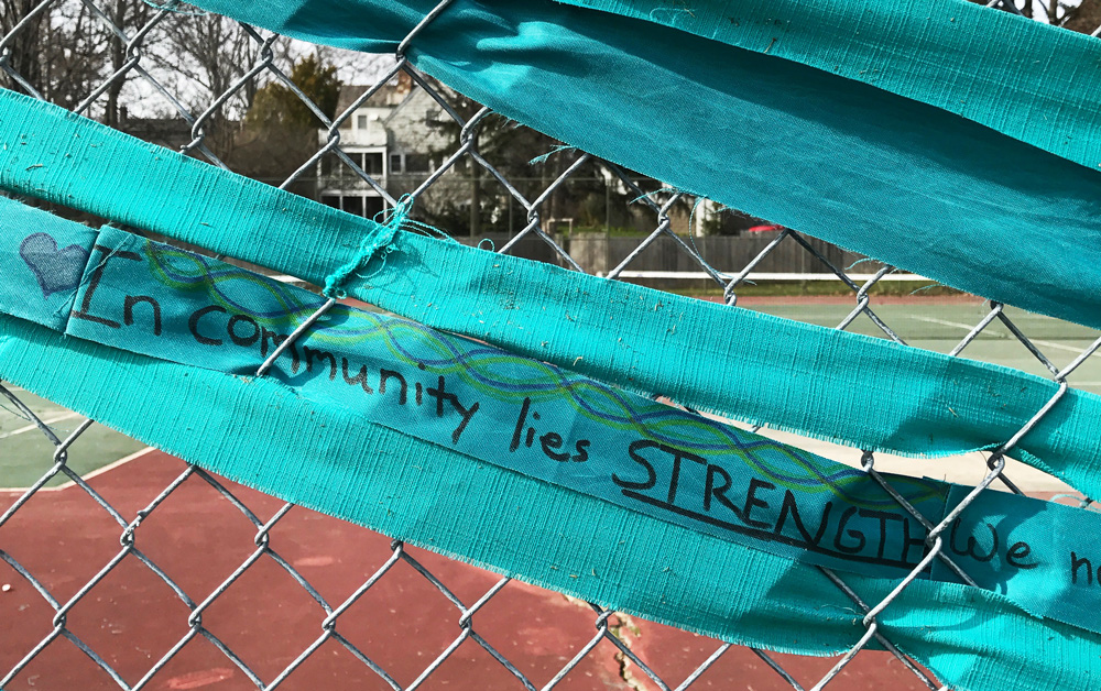 teal cloth woven through fence with the words In community lie strength