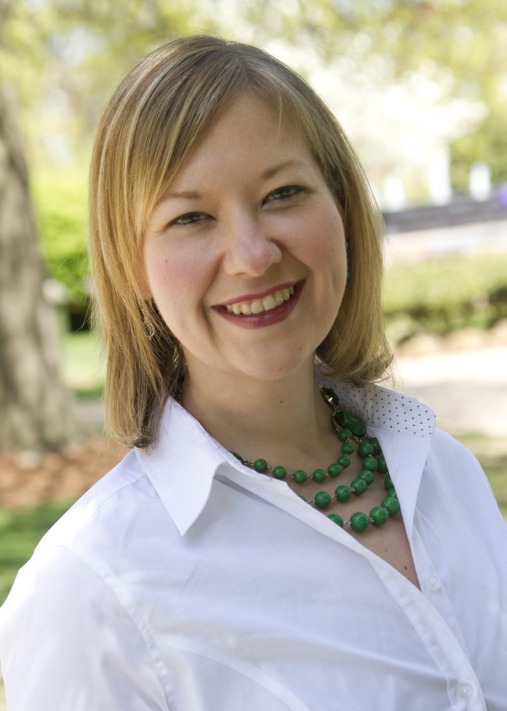 women with short blonde hair wearing a white shirt with a green necklace 