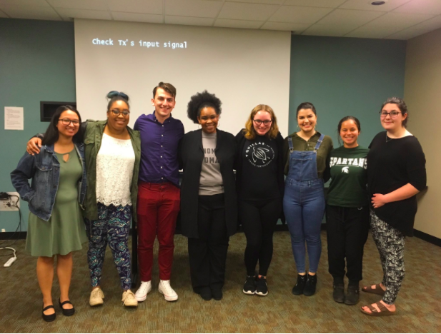 A group of 7 students and one adult are smiling together with their arms around each other.